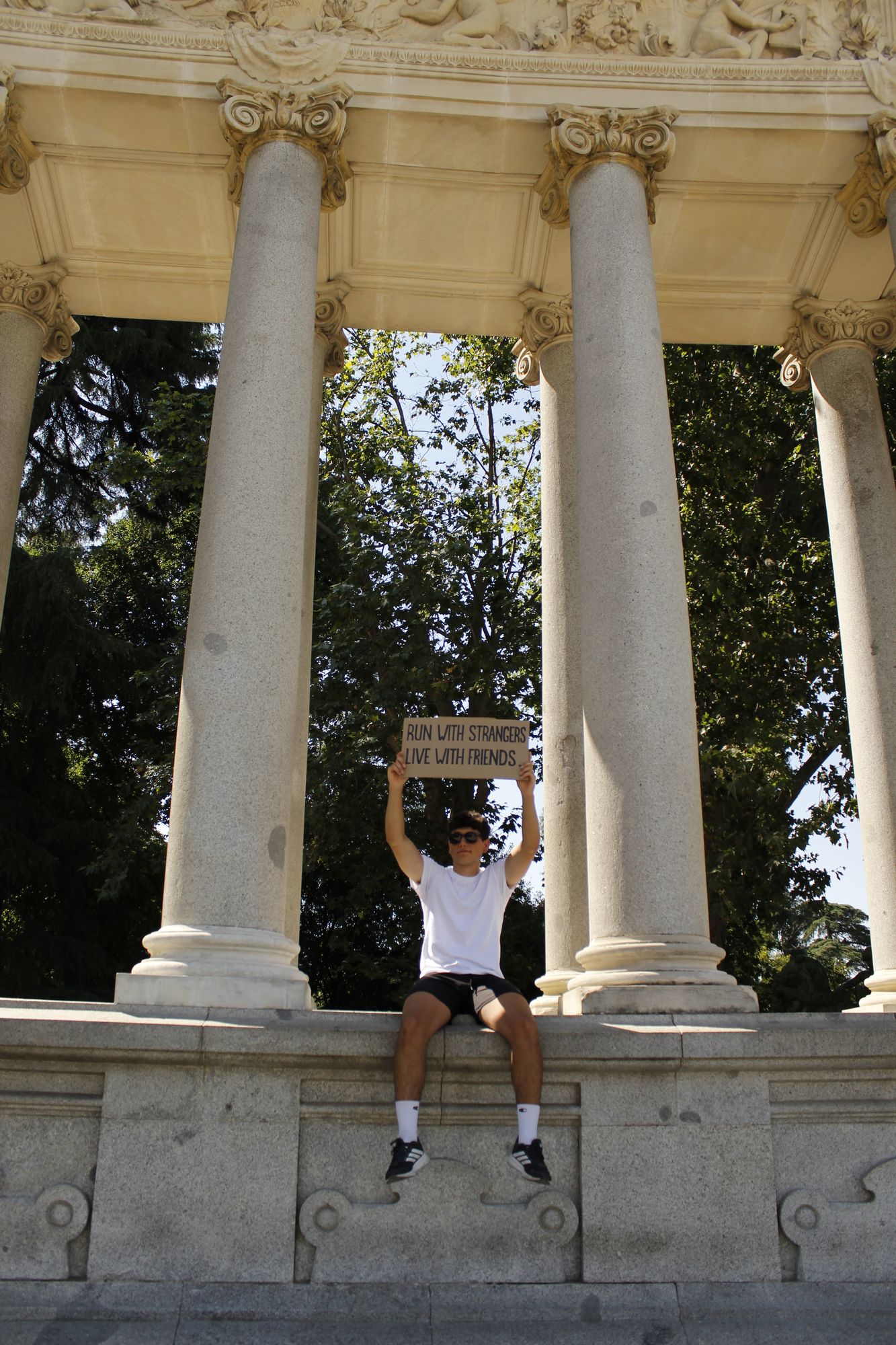 Miembro de Inner Club sosteniendo el cartel Run with strangers, live with friends en la columnata del Retiro